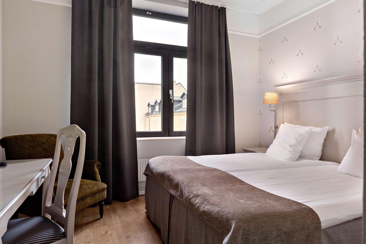 A hotel room with a bed, a chair, a desk, and a window with curtains.