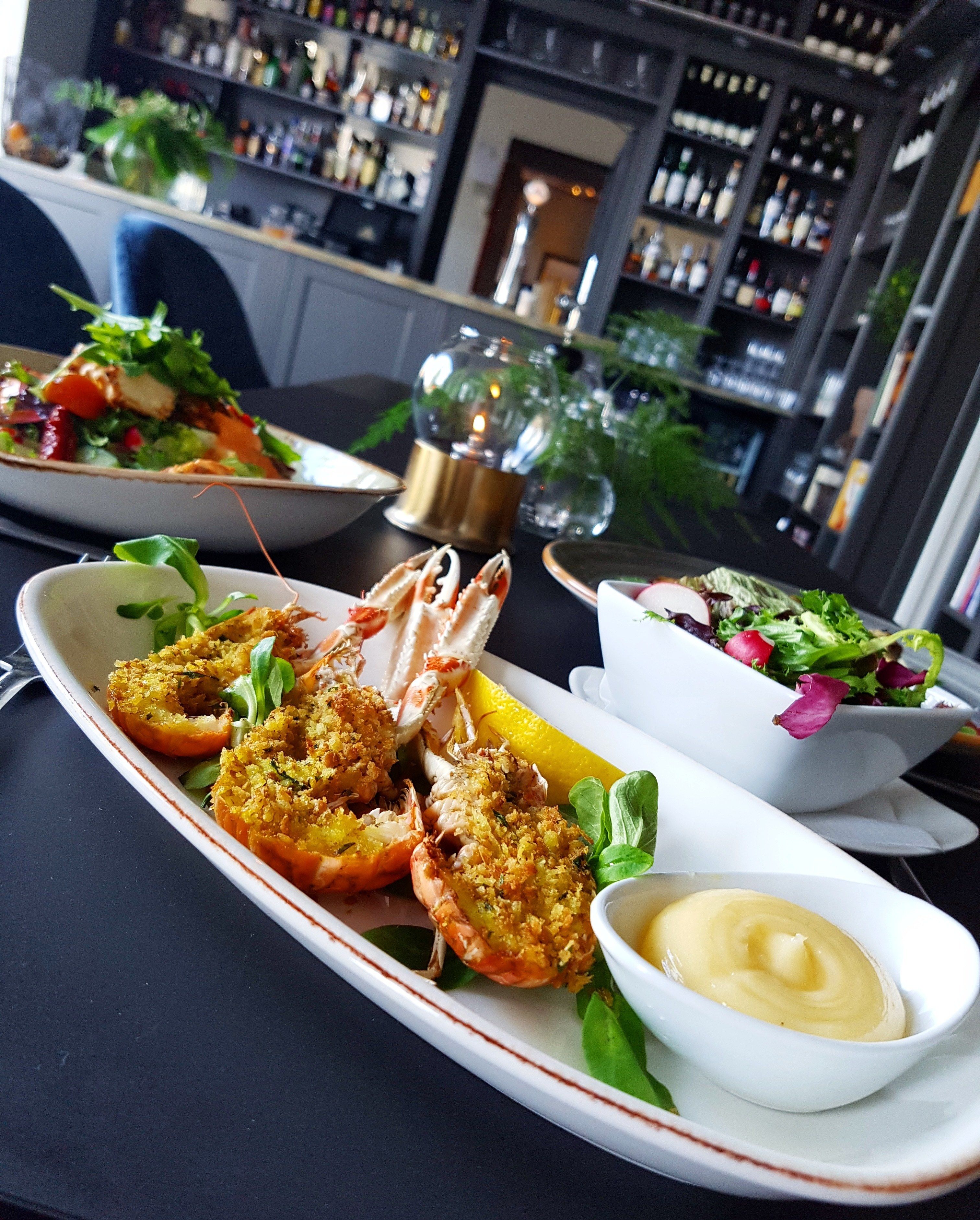 A seafood dish with a side of salad and sauce, set on a table in a restaurant with a bar in the background.