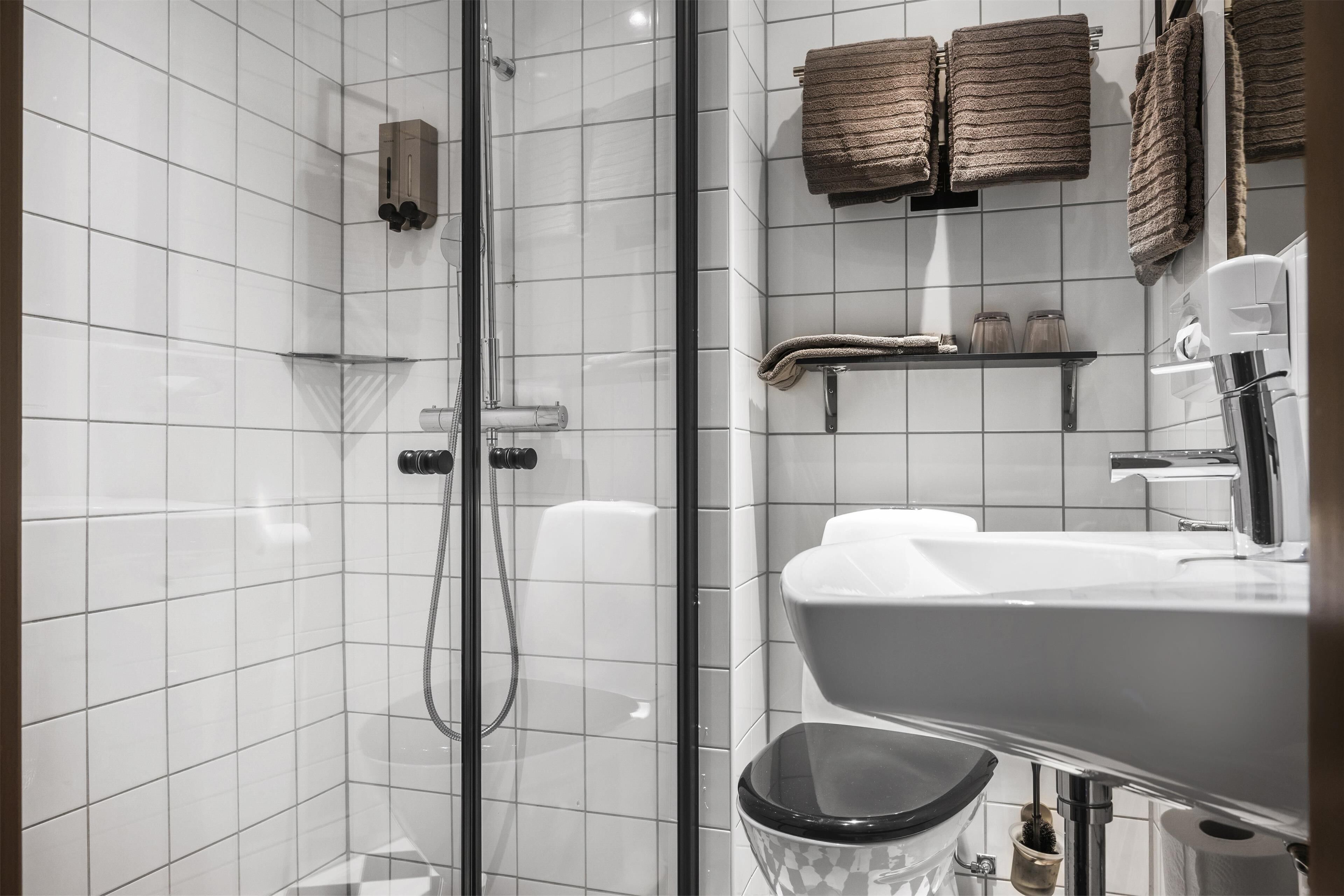 A modern bathroom with a glass shower enclosure, white tiles, a black toilet, and a sink with a mirror.