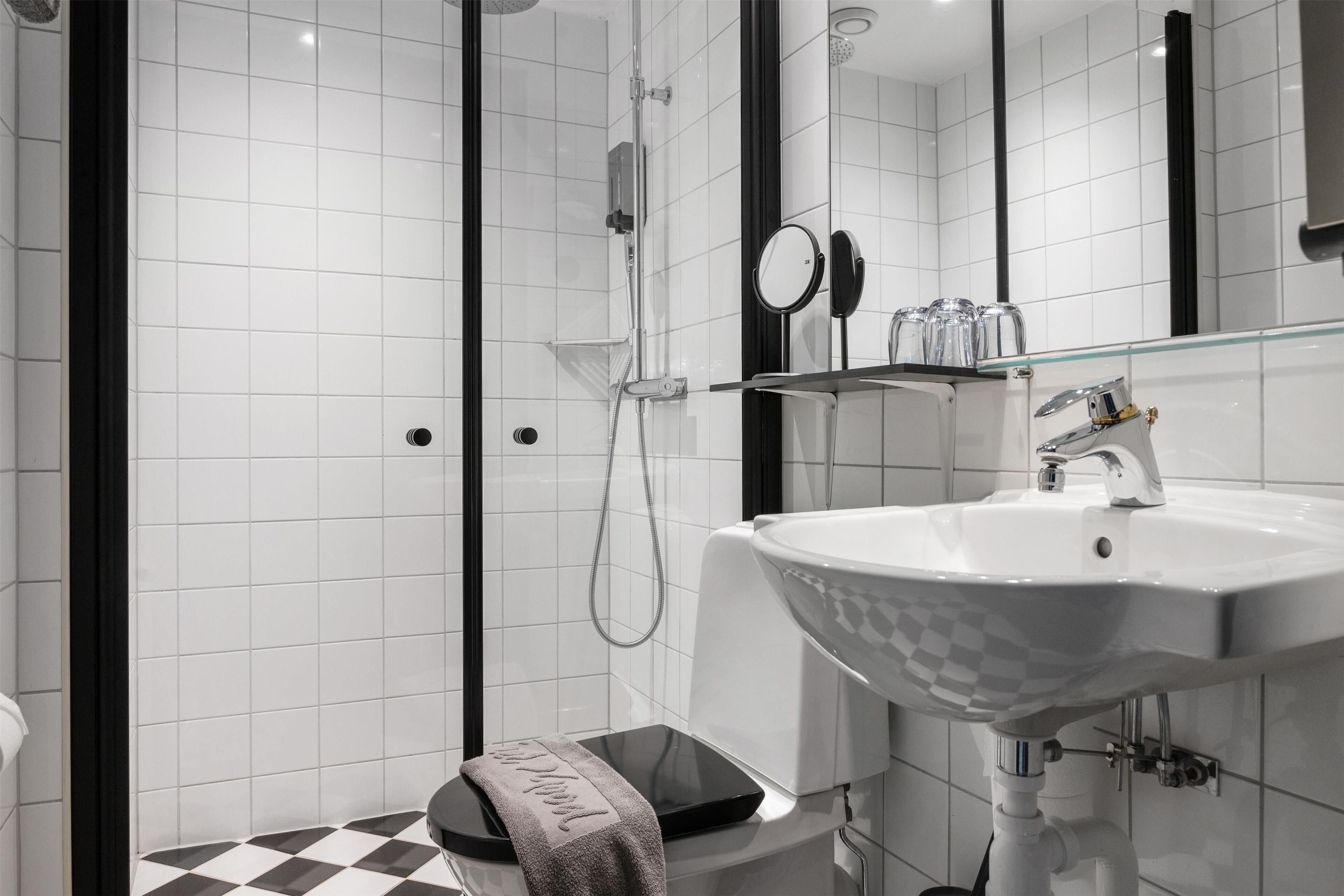 Une salle de bain moderne avec une douche à l’italienne en verre, un lavabo blanc au motif original et des toilettes noires.