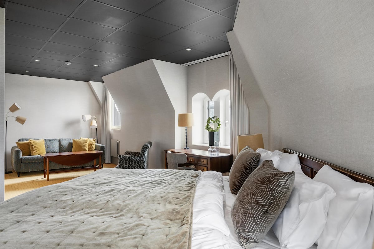 A modern hotel room with a large bed, a sofa, a desk, and a chair.
