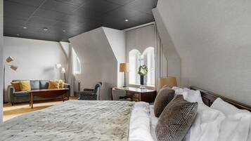 A modern hotel room with a large bed, a sofa, a desk, and a chair.
