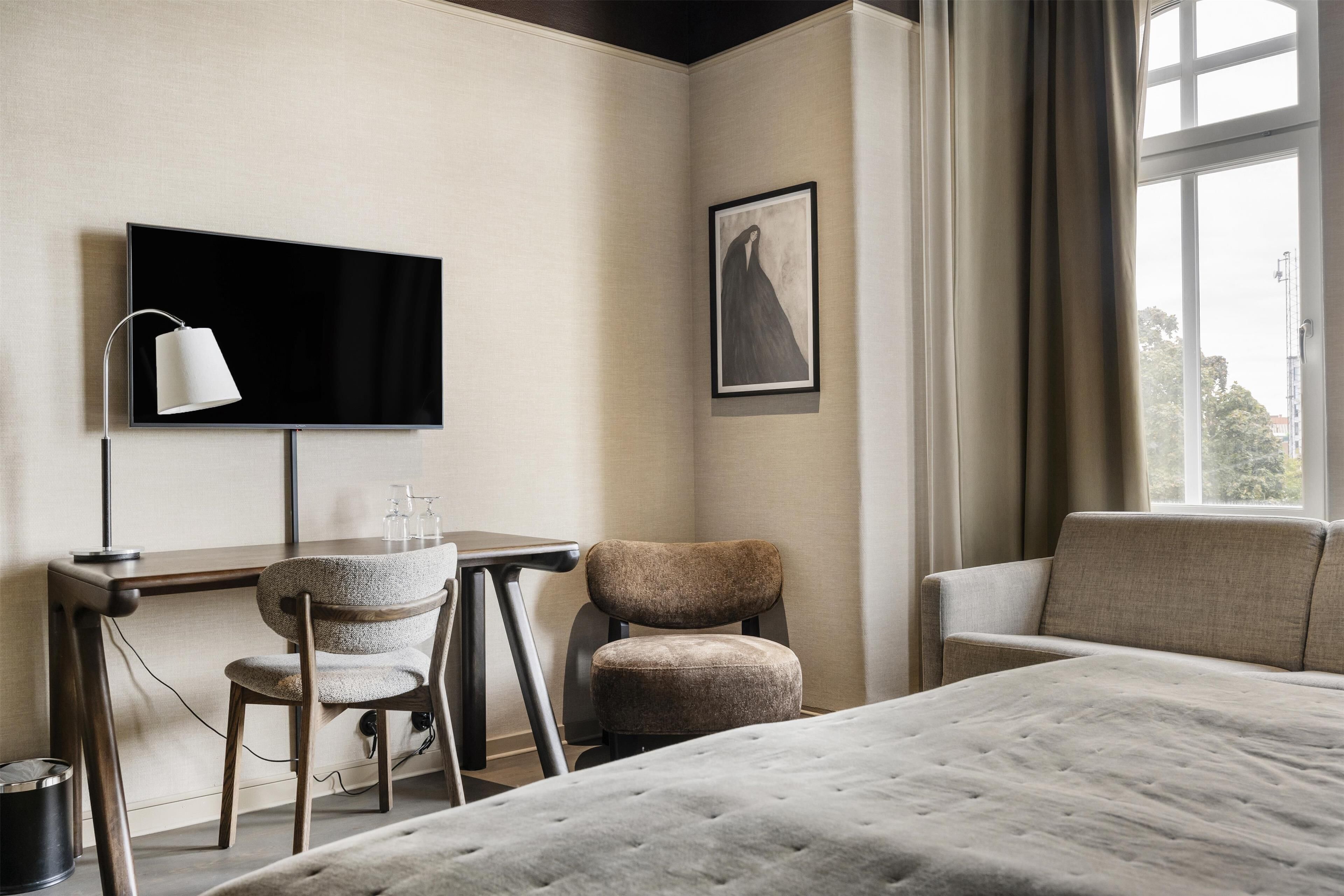 Habitación de hotel con cama, escritorio, silla, televisor y un cuadro en la pared.