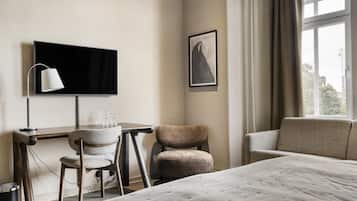 A hotel room with a bed, a desk with a chair, a television, and a framed picture on the wall.