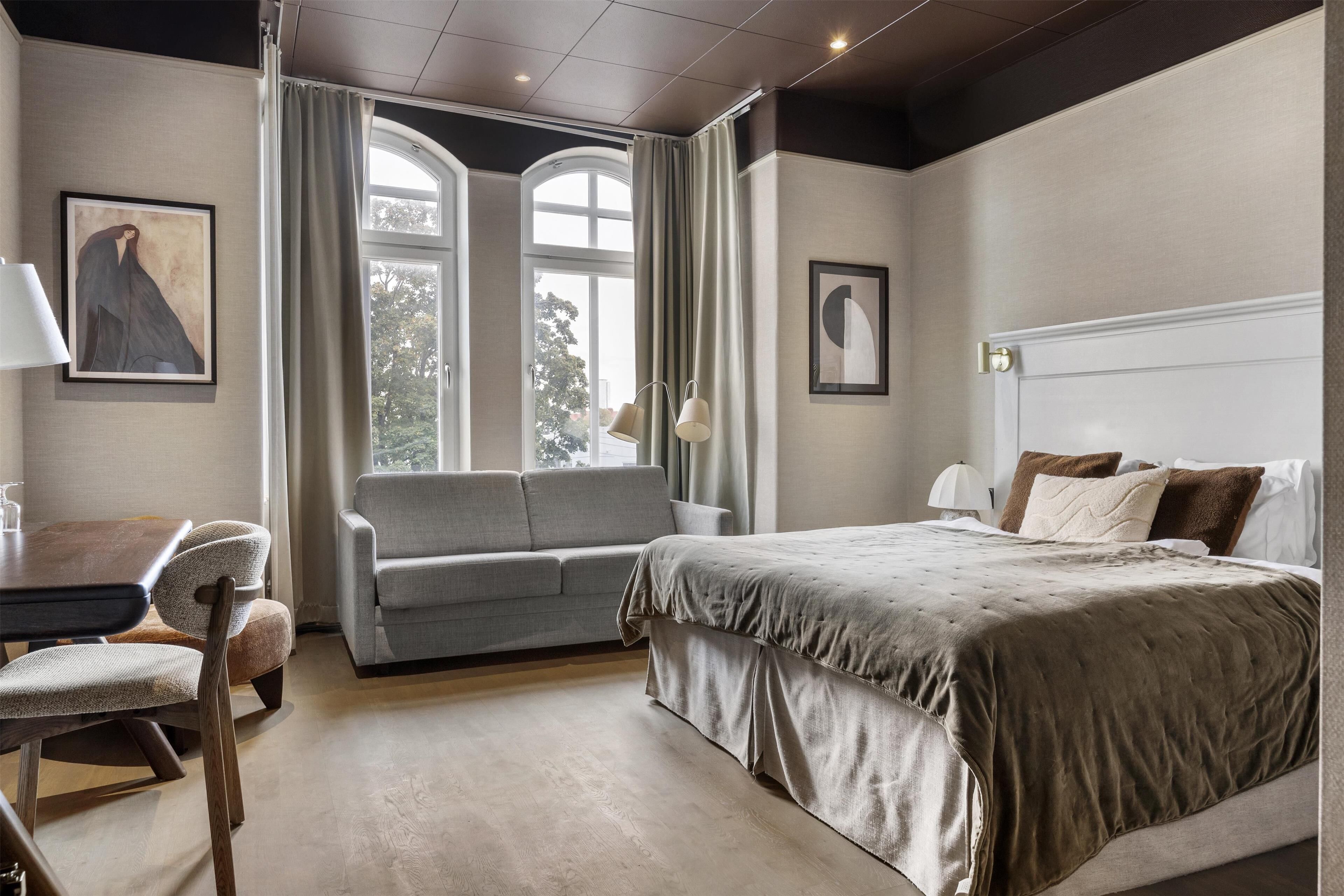 A bedroom with a bed, a sofa, a desk, and a window with curtains.