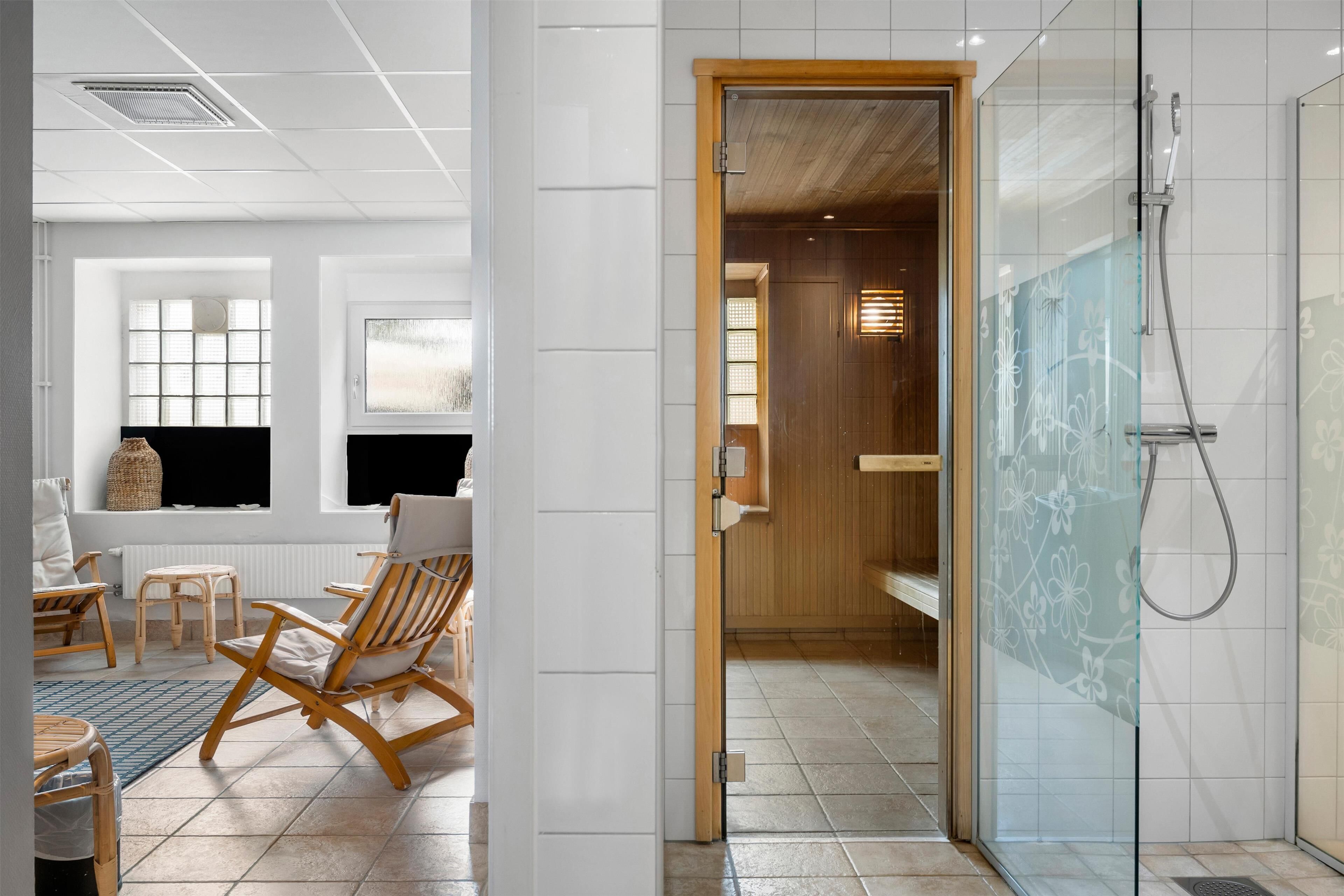 A modern bathroom with a glass shower enclosure, wooden flooring, and a seating area with chairs and a table.