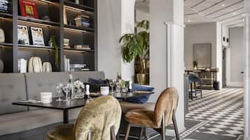 Una sala de estar moderna con un sofá gris, dos sillones de terciopelo, una mesa de centro y una estantería llena de libros y objetos decorativos.