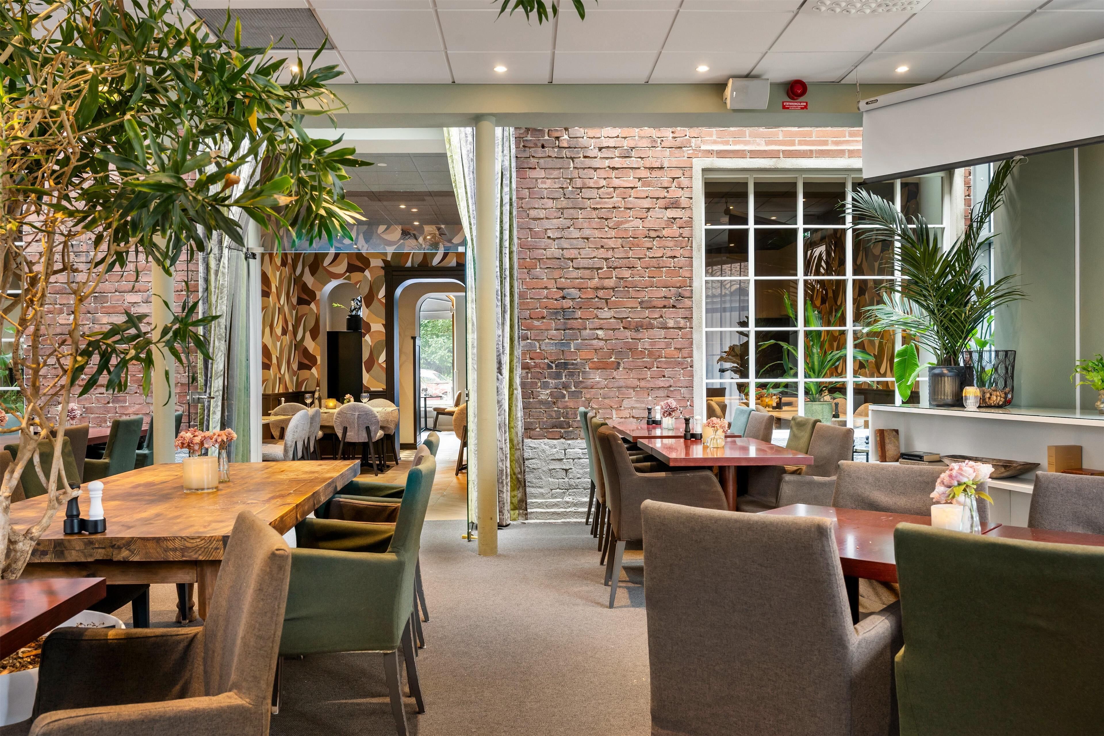 Een restaurant met bakstenen muren, houten tafels en groene stoelen.