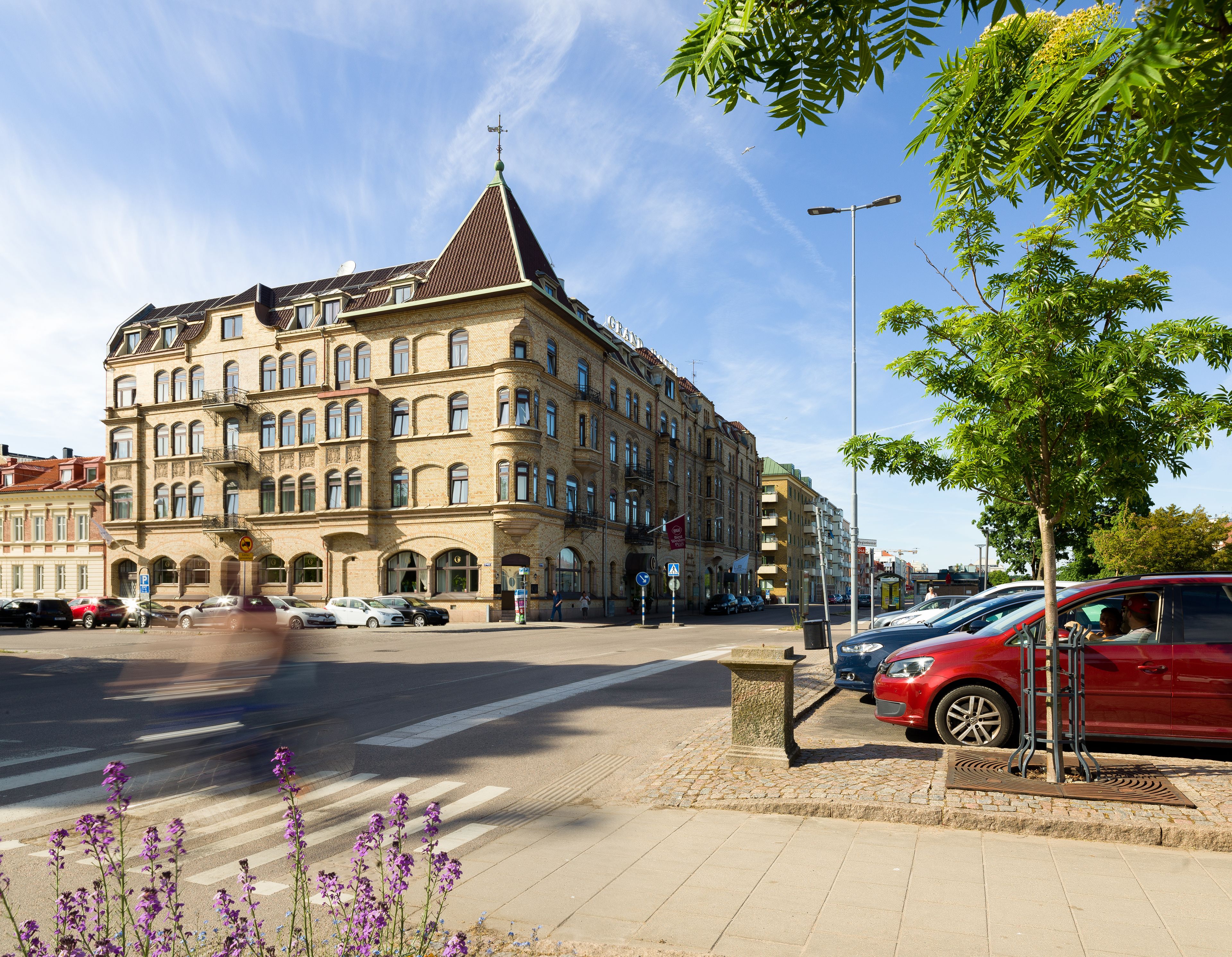 En byggnad med flera våningar, ett markant hörntorn, stora fönster och en entré i markplan.