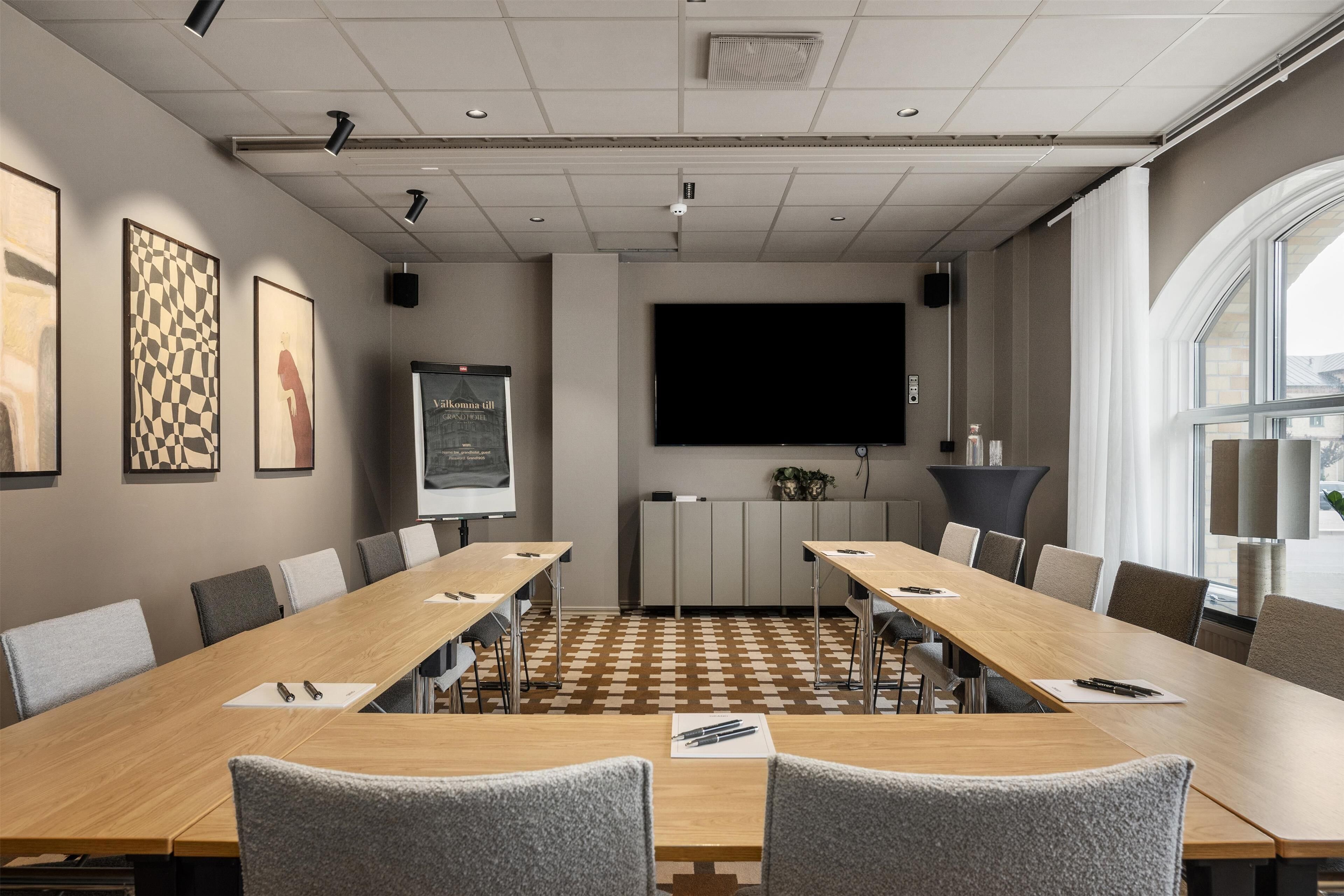 A conference room with a long table, chairs, a projector screen, and framed artwork on the walls.