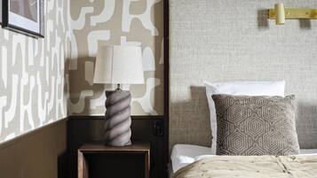 A neatly made bed with a patterned pillow, a bedside lamp on a wooden nightstand, and a wall with a geometric pattern.