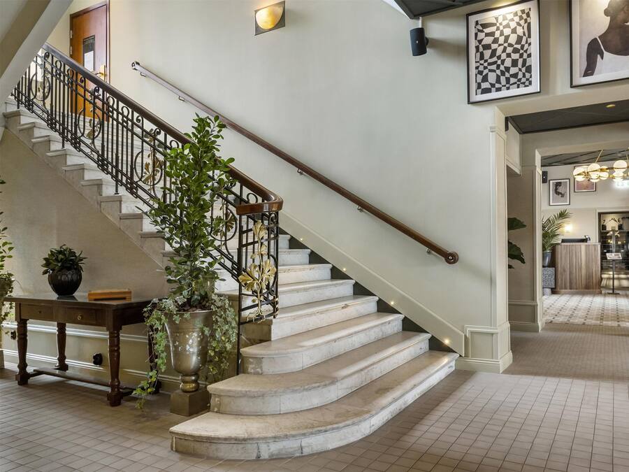Una imponente escalera de madera con barandilla y balaustradas de metal, que conduce a un rellano con una planta en maceta y una pequeña mesa.