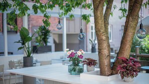 An outdoor seating area with a white table, potted plants, hanging light fixtures, and a tree trunk. - Grand Halmstad, WorldHotels Crafted (Halmstad)