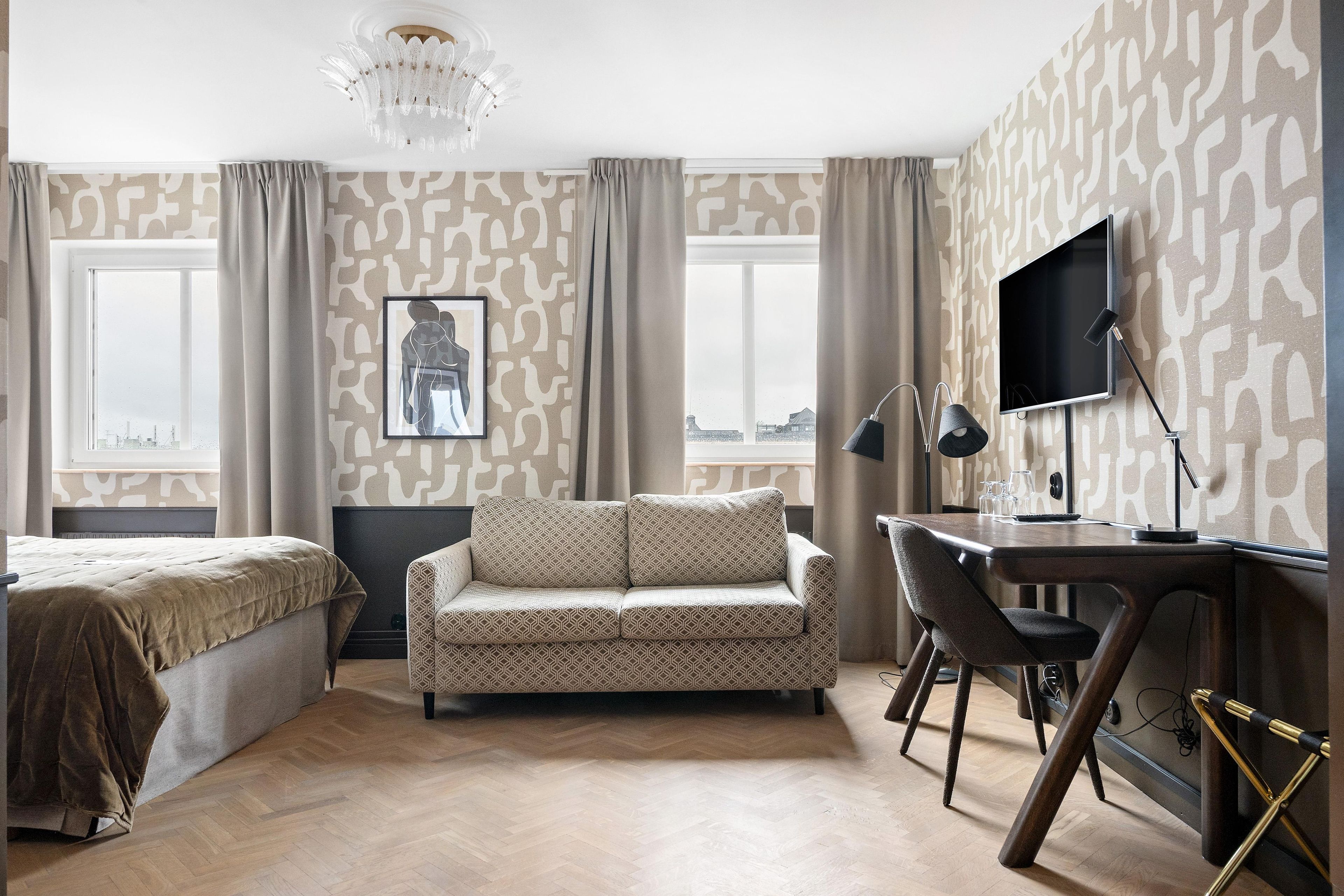 A hotel room with a bed, a sofa, a desk with a computer, and a TV.