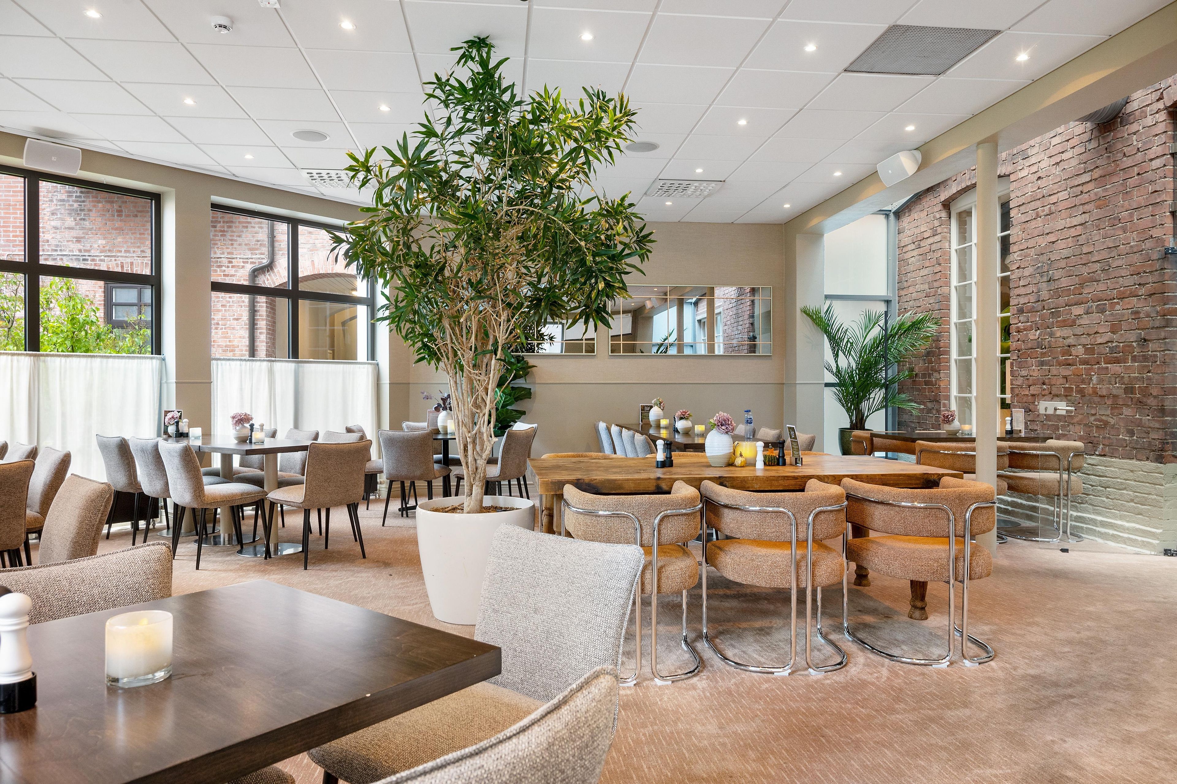 Un vaste espace dédié à la salle à manger, avec plusieurs tables et chaises, une grande plante en pot et un mur en briques.