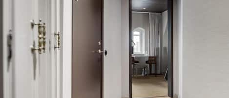A hallway with a wooden floor leading to a room with a dining area, a window with curtains, and a view of the city.