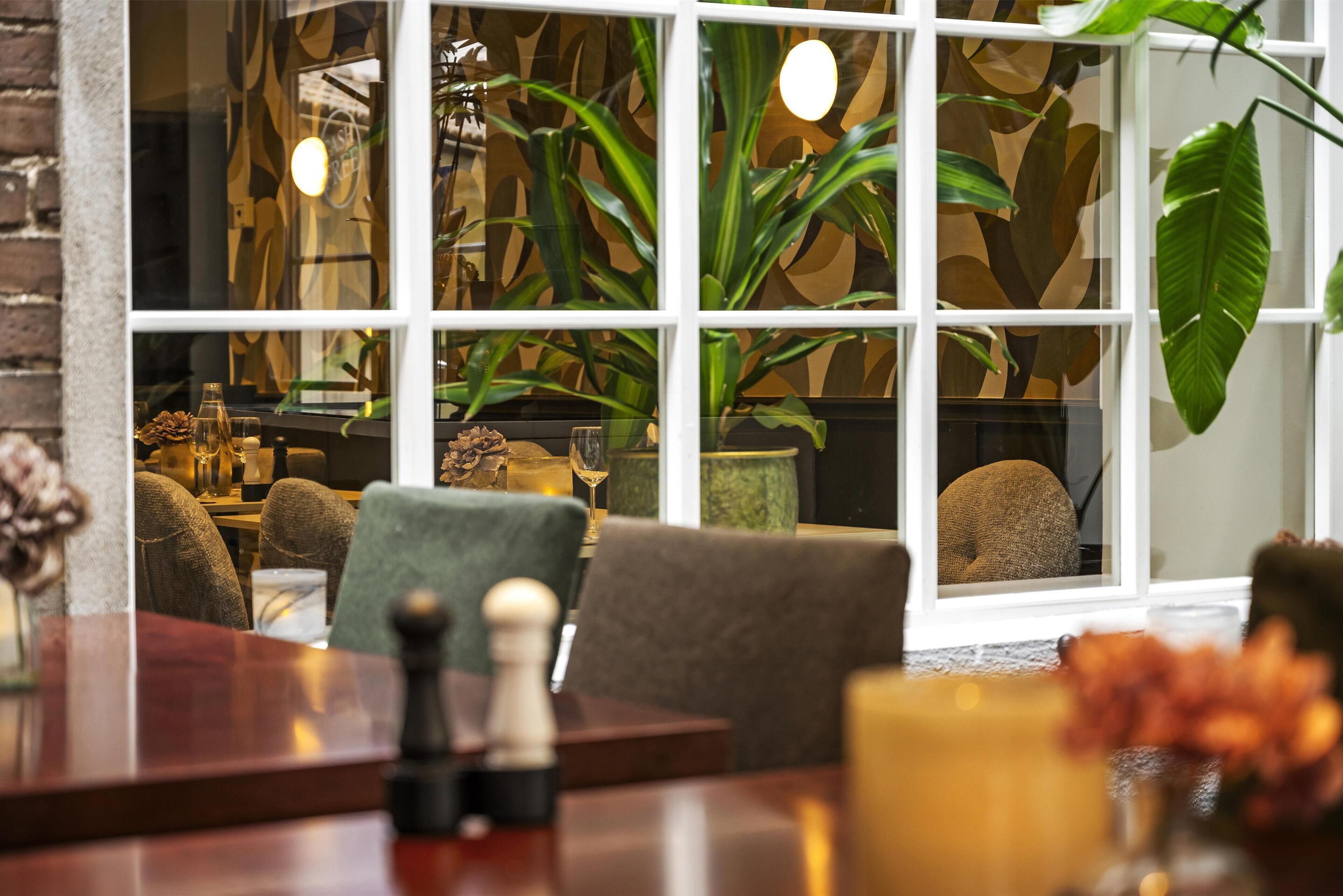 A cozy interior with a wooden table, chairs, and a large window with a view of indoor plants.