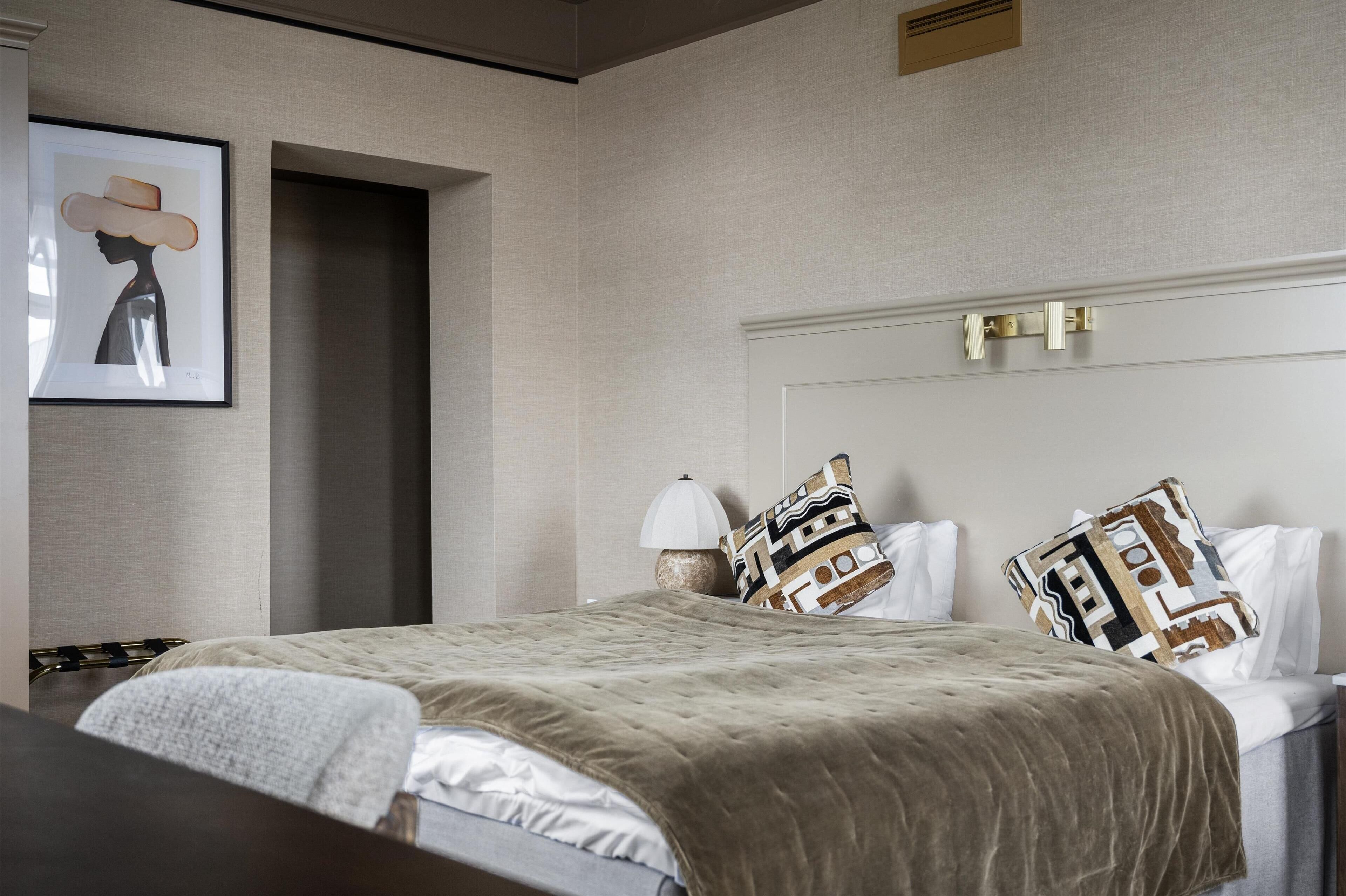 A hotel room with a bed, a bedside table, a lamp, and a framed artwork on the wall.