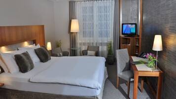 Une chambre d’hôtel avec un lit, deux chaises, un bureau avec une lampe, une télévision et une plante en pot.
