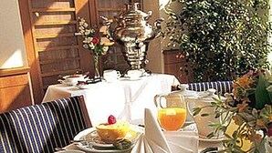 Mesa posta para o café da manhã com pão, uma fruta, uma xícara e um jarro de suco de laranja.
