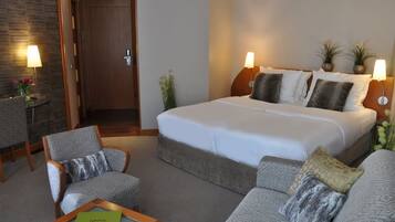 Ein Hotelzimmer mit einem großen Bett, zwei Nachttischlampen, einem Sofa, einem Sessel und einem kleinen Tisch.