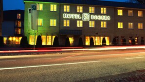 Um hotel com uma placa grande indicando "HOTEL EGGERS" e uma fachada iluminada em verde.