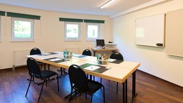 A conference room with a long table, six chairs, a whiteboard, and three windows with green curtains.