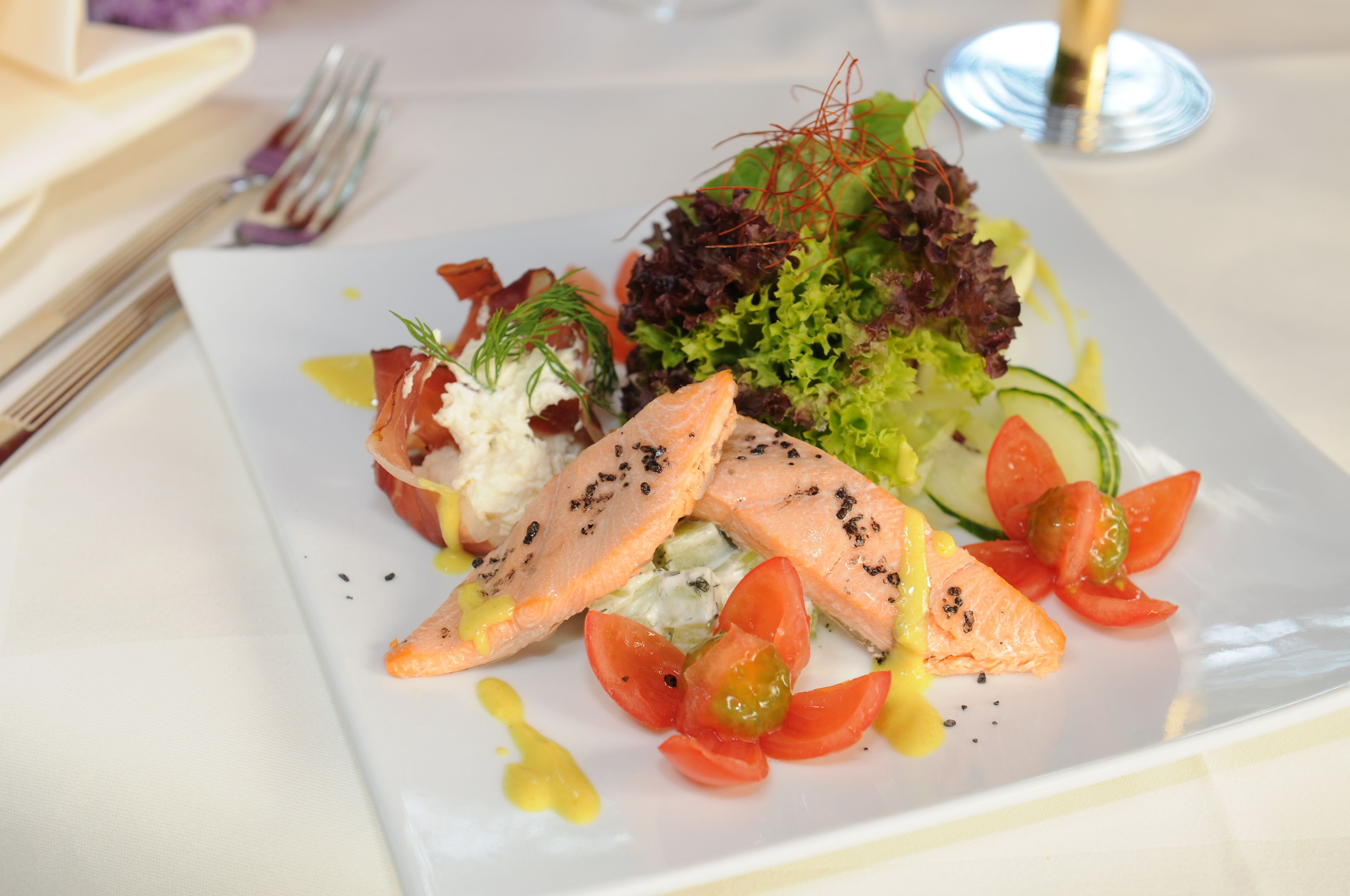 Ein quadratischer Teller mit Salat, Lachs und einer dekorativen Soße.