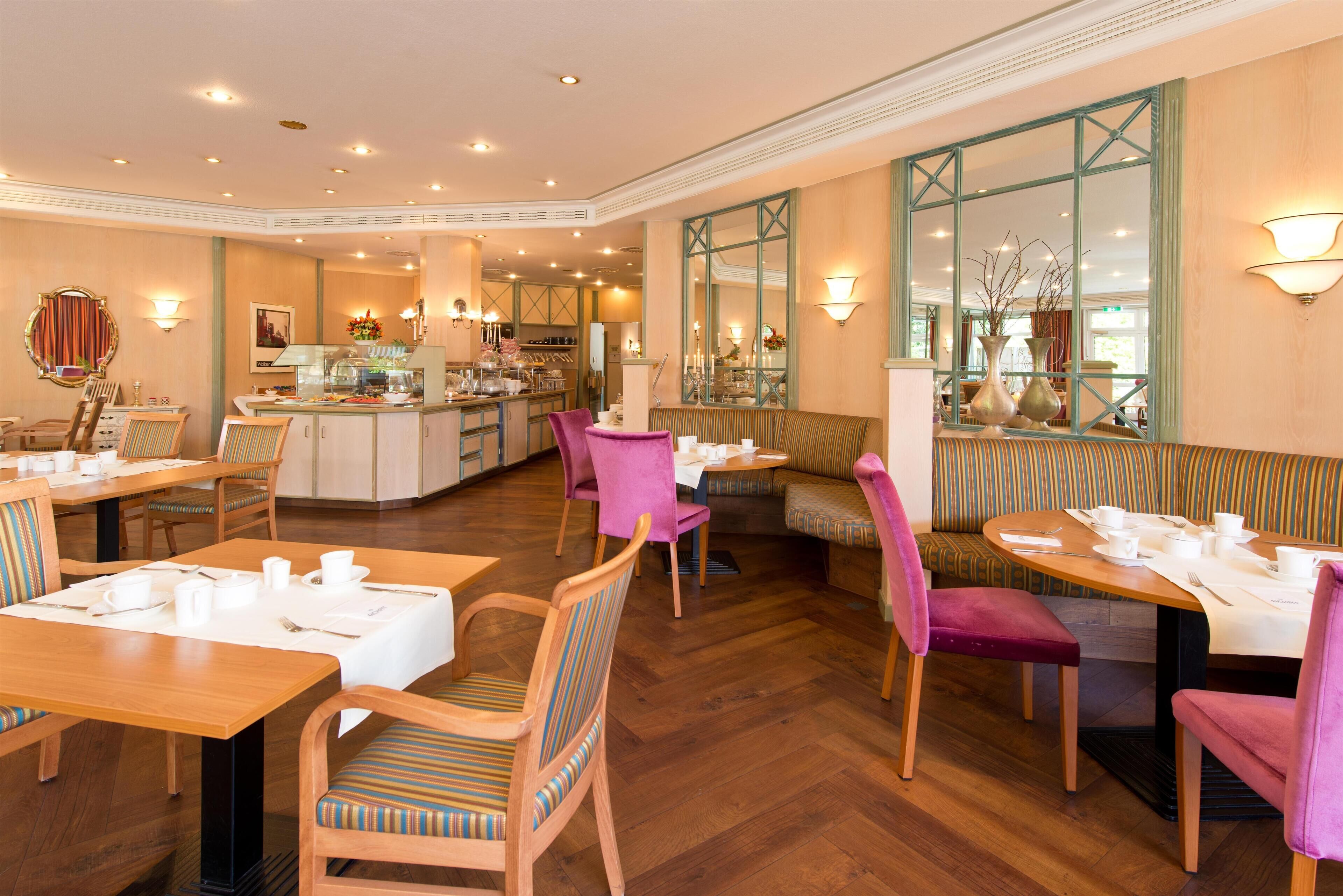 A hotel dining area with wooden tables, cushioned chairs, and a central bar area.
