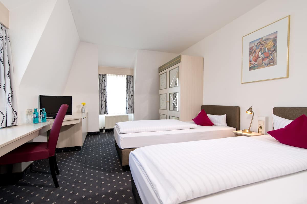 A hotel room with two beds, a desk, a chair, a TV, and a window with curtains.