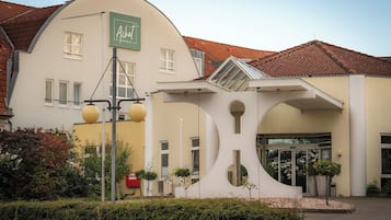 Ein Hotel mit einer geschwungenen Fassade, einem grünen Schild und einem modernen Eingang mit runden Ausschnitten.