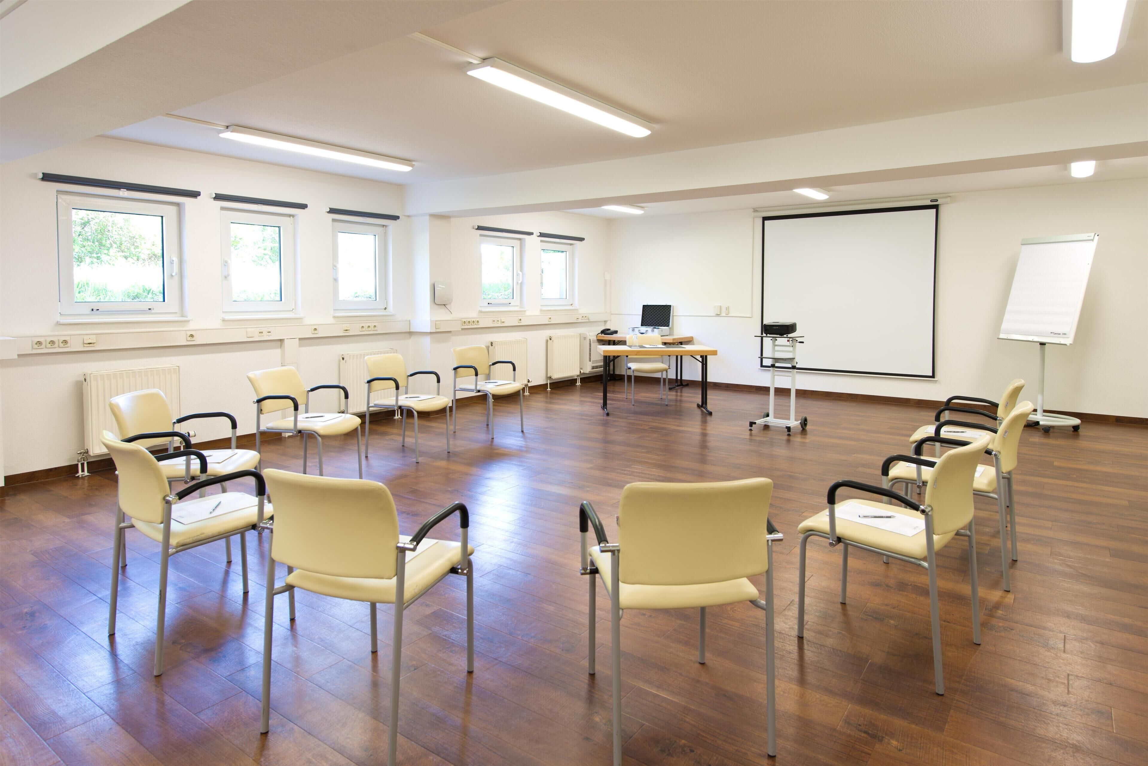 Ein Konferenzraum mit großem Bildschirm, mehreren Stühlen und einer Whiteboard-Tafel.