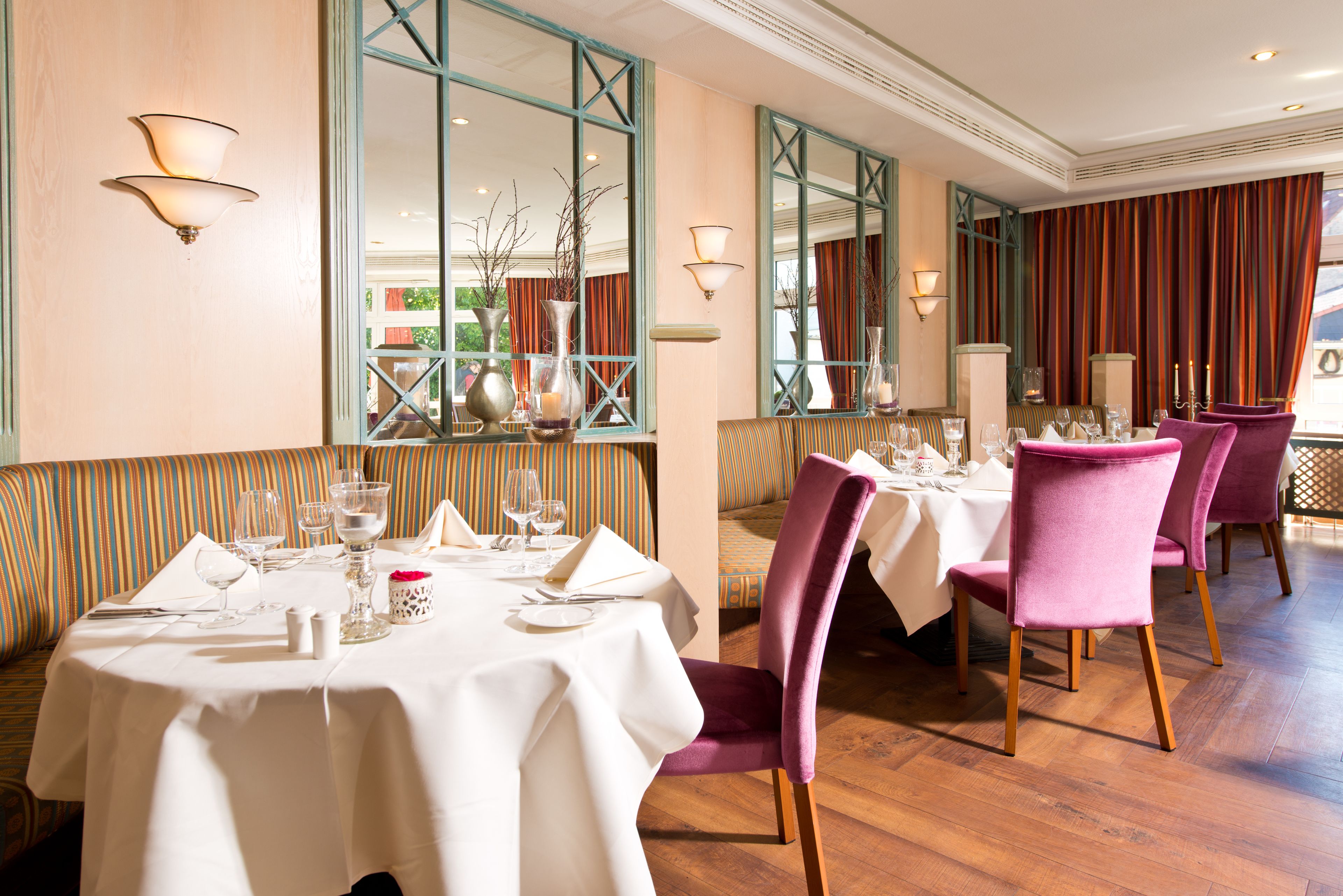 Un ristorante con tavoli apparecchiati, sedute a righe e ampie finestre con tende.