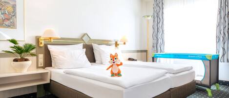 A hotel room with a bed, a nightstand with a lamp, a desk, a chair, a window with curtains, and a small plant.