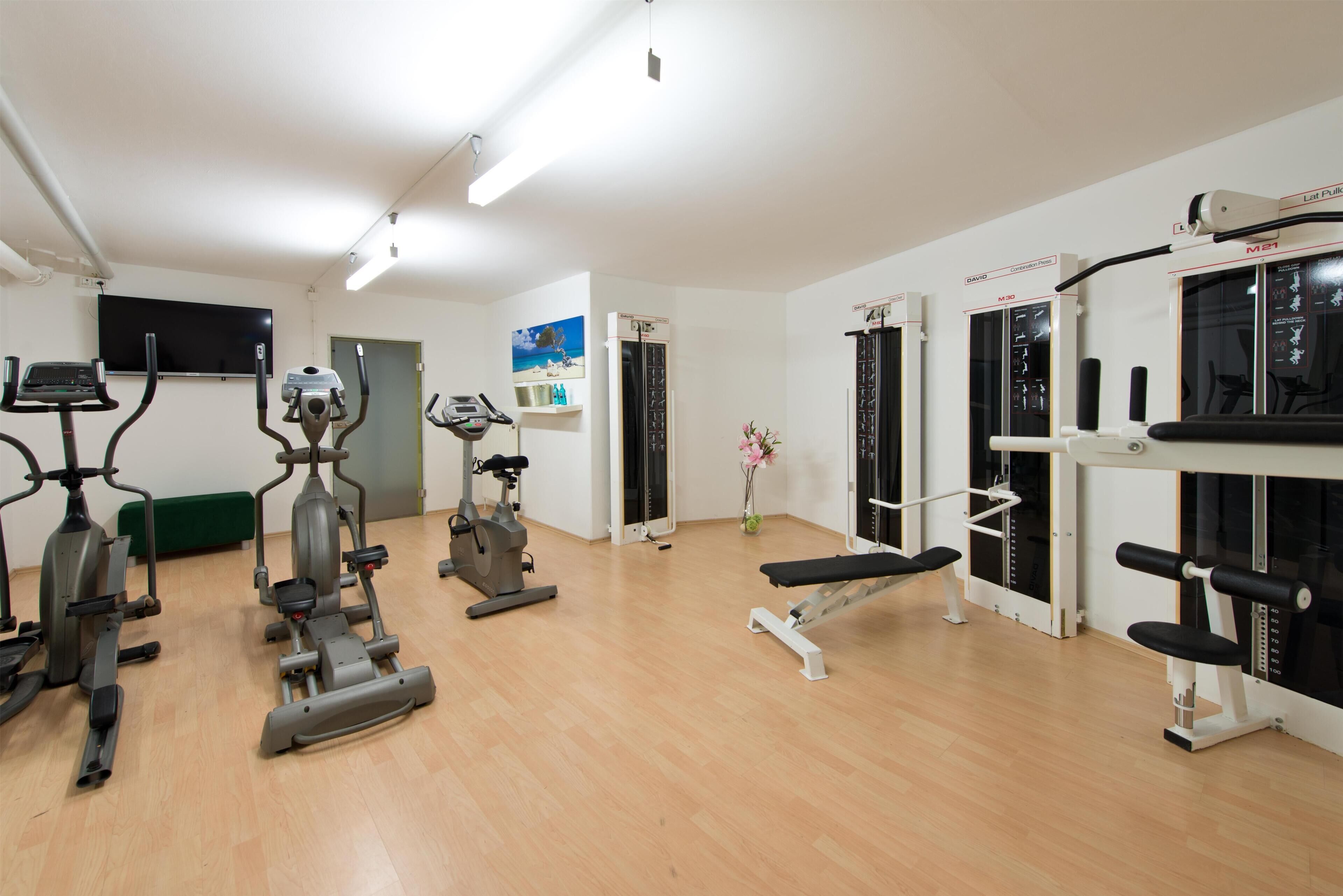 A gym with various exercise machines, a bench, and a television on the wall.