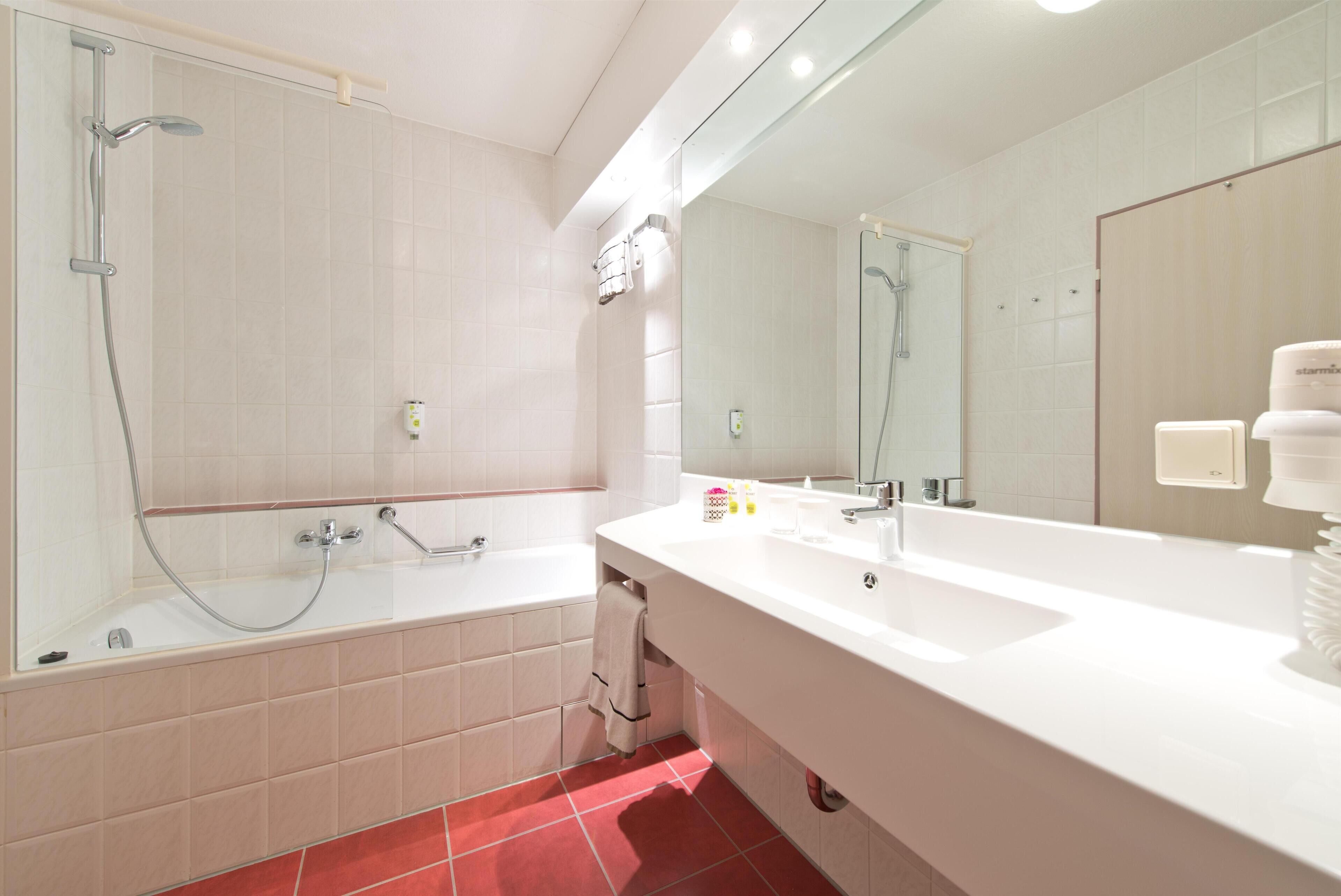 A modern bathroom with a large mirror, a bathtub, and a shower.