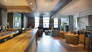 A modern bar area with a wooden counter, seating with cushions, and large windows providing natural light. - Scandic Helsinki Aviacongress (Vantaa)