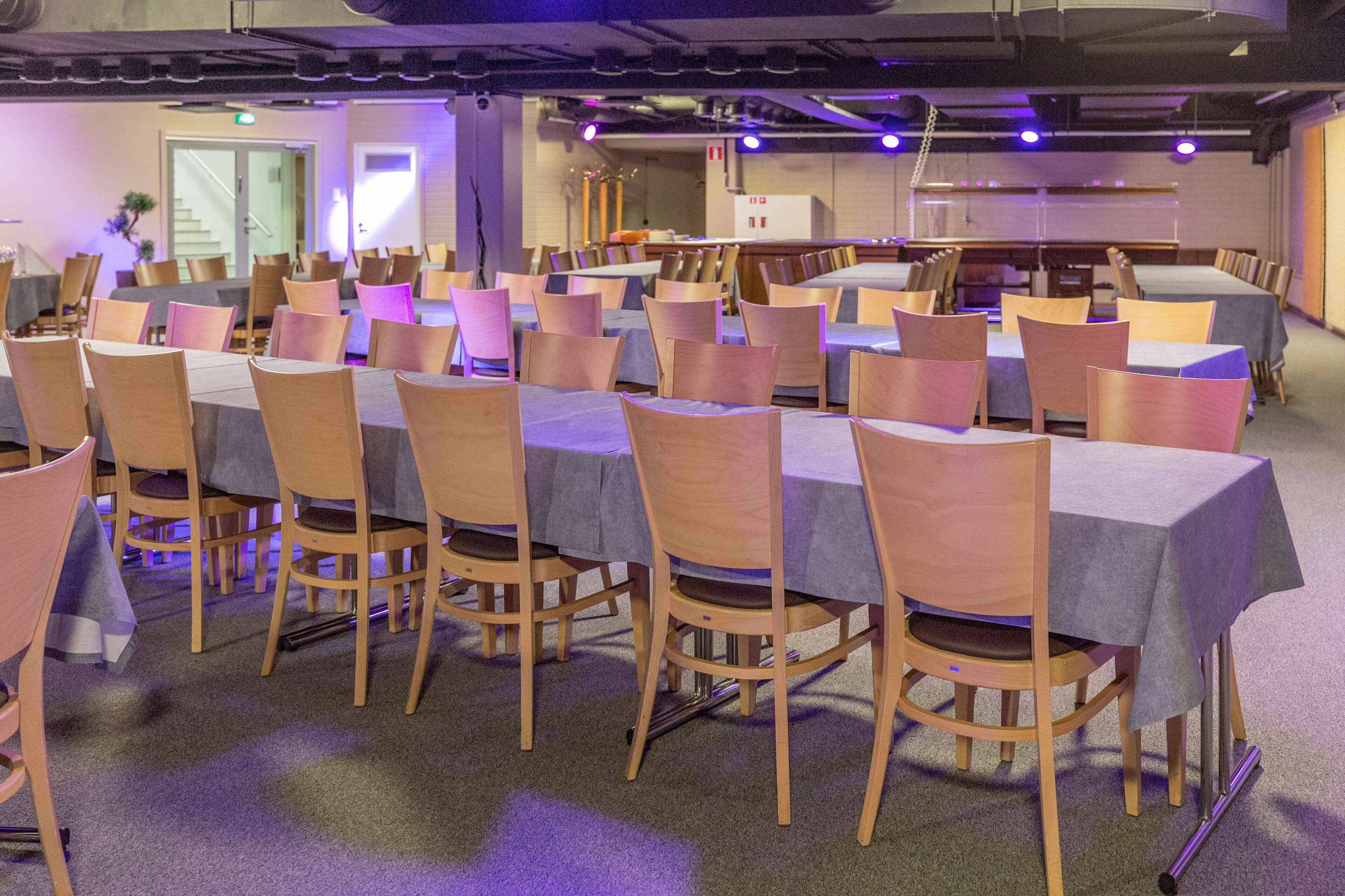 Ein Konferenzraum mit mehreren Tischen und Stühlen, ausgestattet mit Tischen, Stühlen und einer Projektionsleinwand.