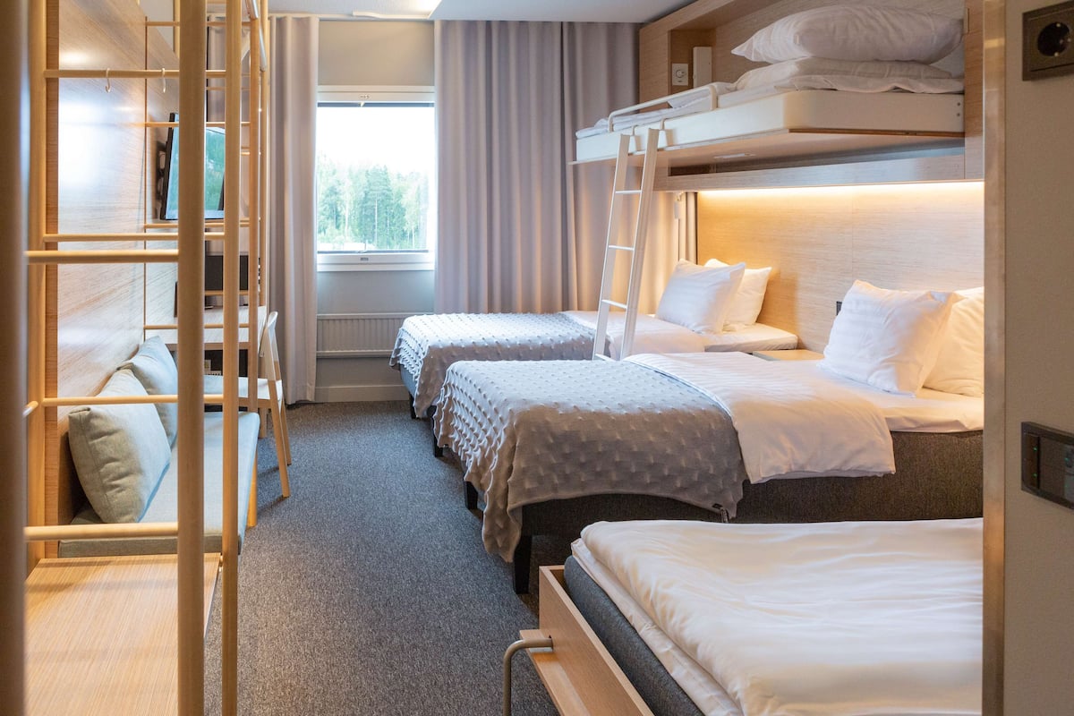A hotel room with bunk beds, a ladder, and a view of trees through a window.