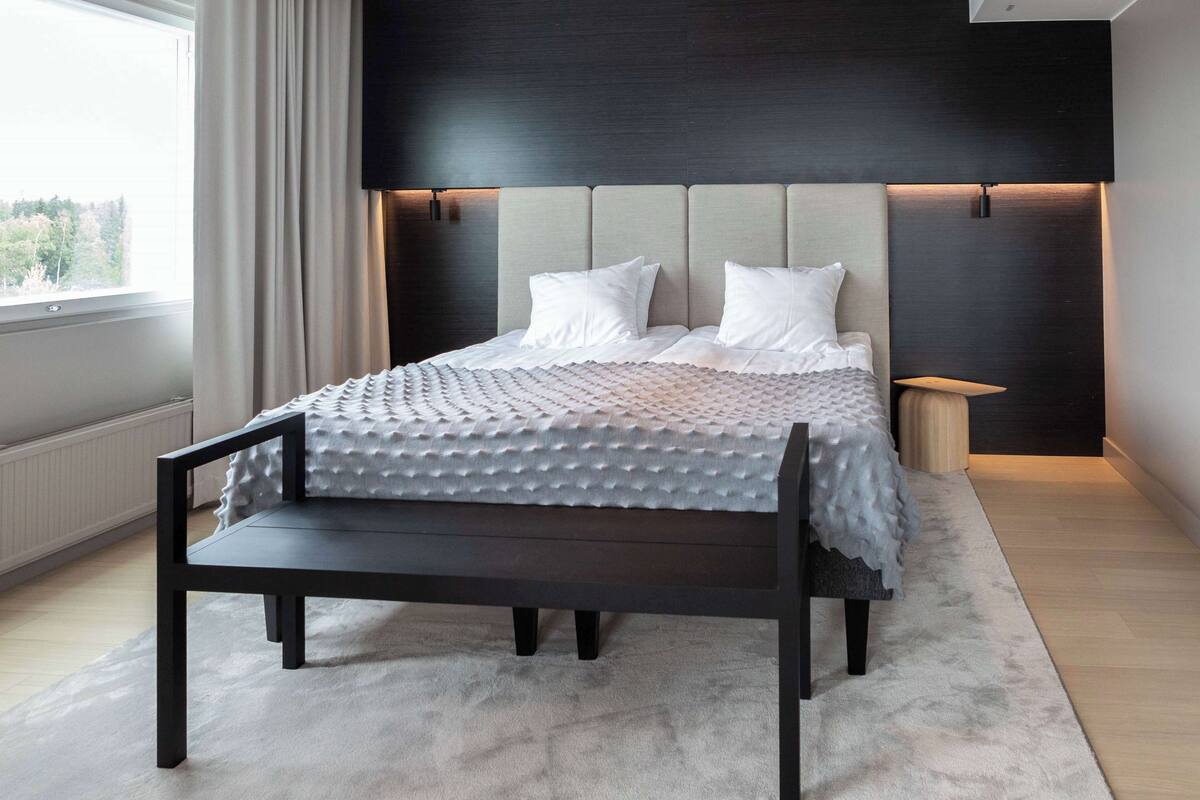 A modern bedroom with a bed, bedside tables, and a view of the outdoors.