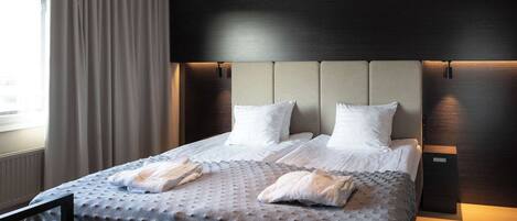 Habitación de hotel moderna con una cama grande, un cabecero con iluminación integrada y vistas a la ciudad desde la ventana.