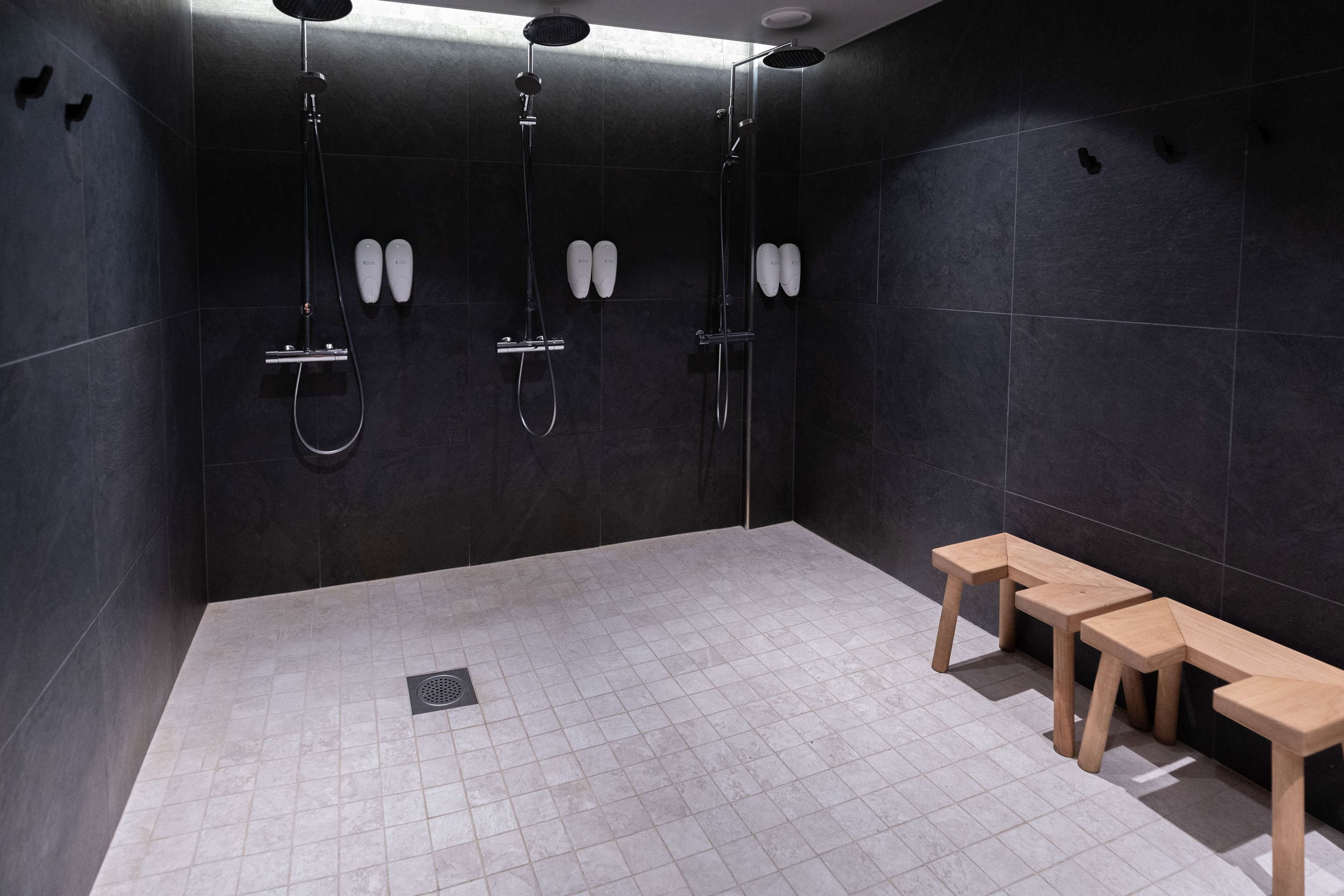 Un espacio de ducha moderno con tres cabezales, un banco y desagüe.