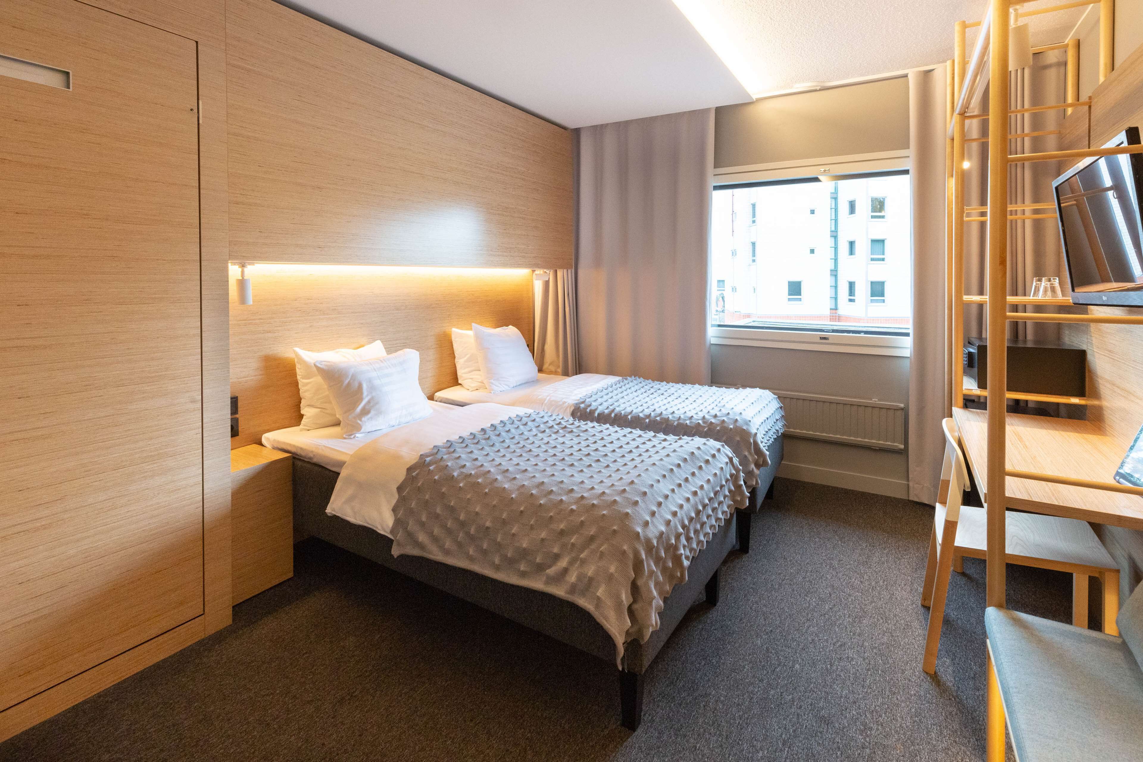 A modern hotel room with two beds, a desk, and a TV.