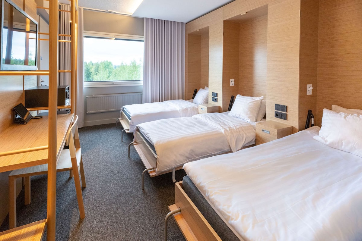 A hotel room with two beds, a desk, a chair, a TV, and a window with curtains.