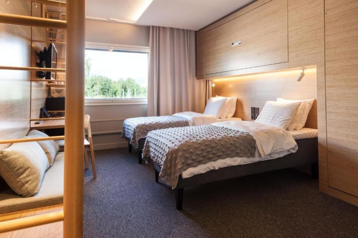 Une chambre d’hôtel avec deux lits, une armoire, un bureau et une fenêtre donnant sur un beau paysage.