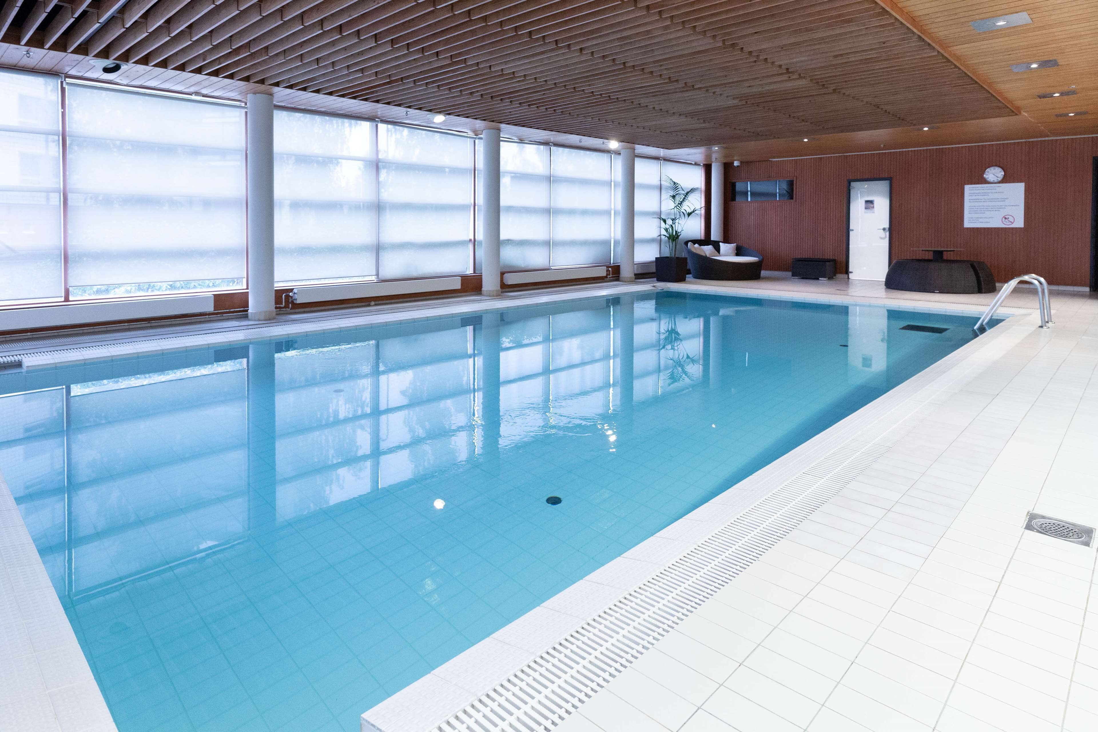 An indoor swimming pool with clear blue water, large windows, and a wooden ceiling.