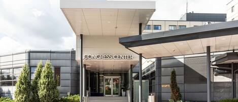 La entrada a un edificio con la leyenda "CONGRESS CENTER", un acceso cubierto, puertas de vidrio y un camino pavimentado.