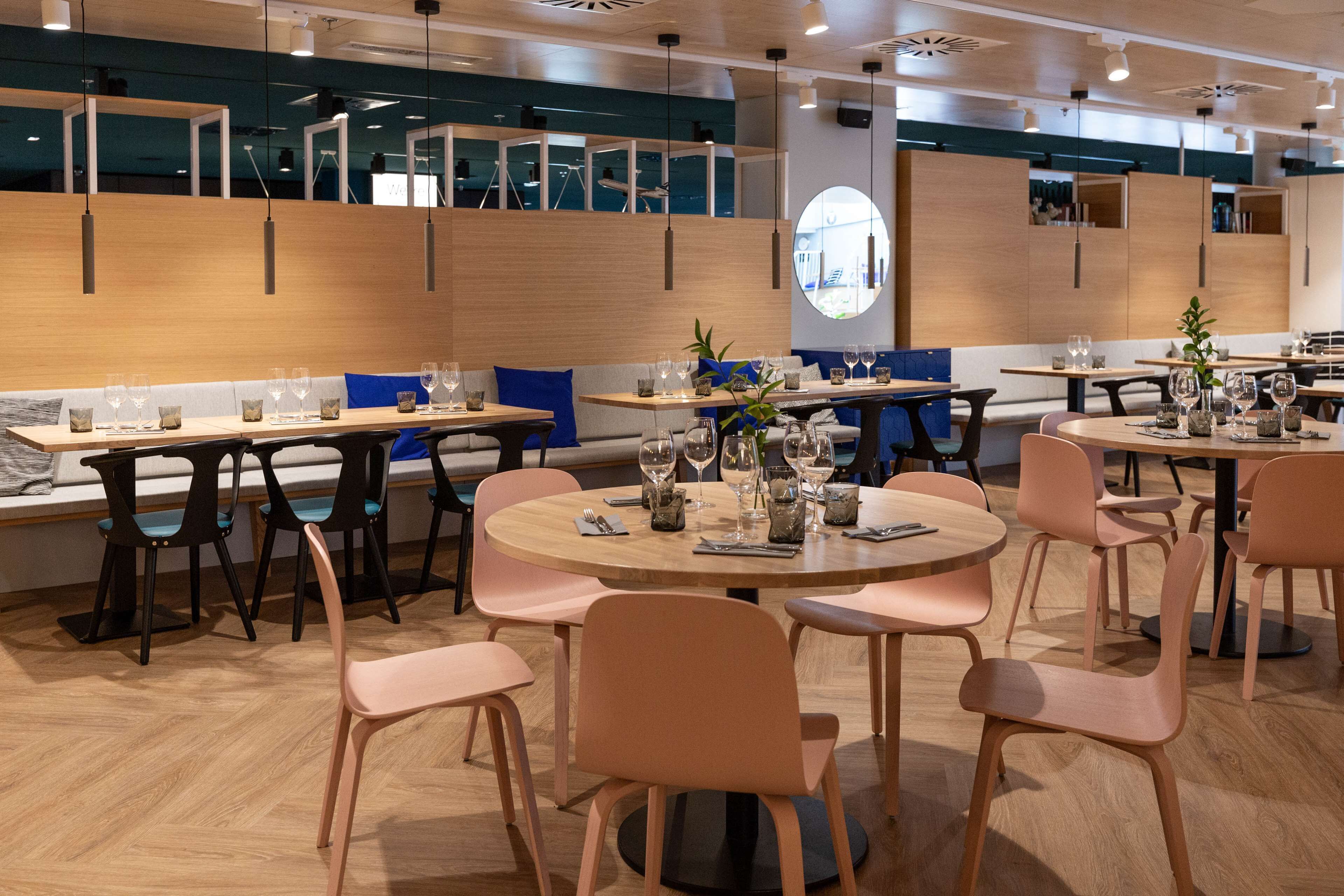 Un restaurante moderno con mesas y sillas redondas, detalles de madera y vistas a la ciudad a través de amplios ventanales.