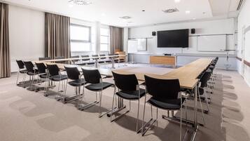 A conference room with a long table, chairs, a whiteboard, and a TV screen.