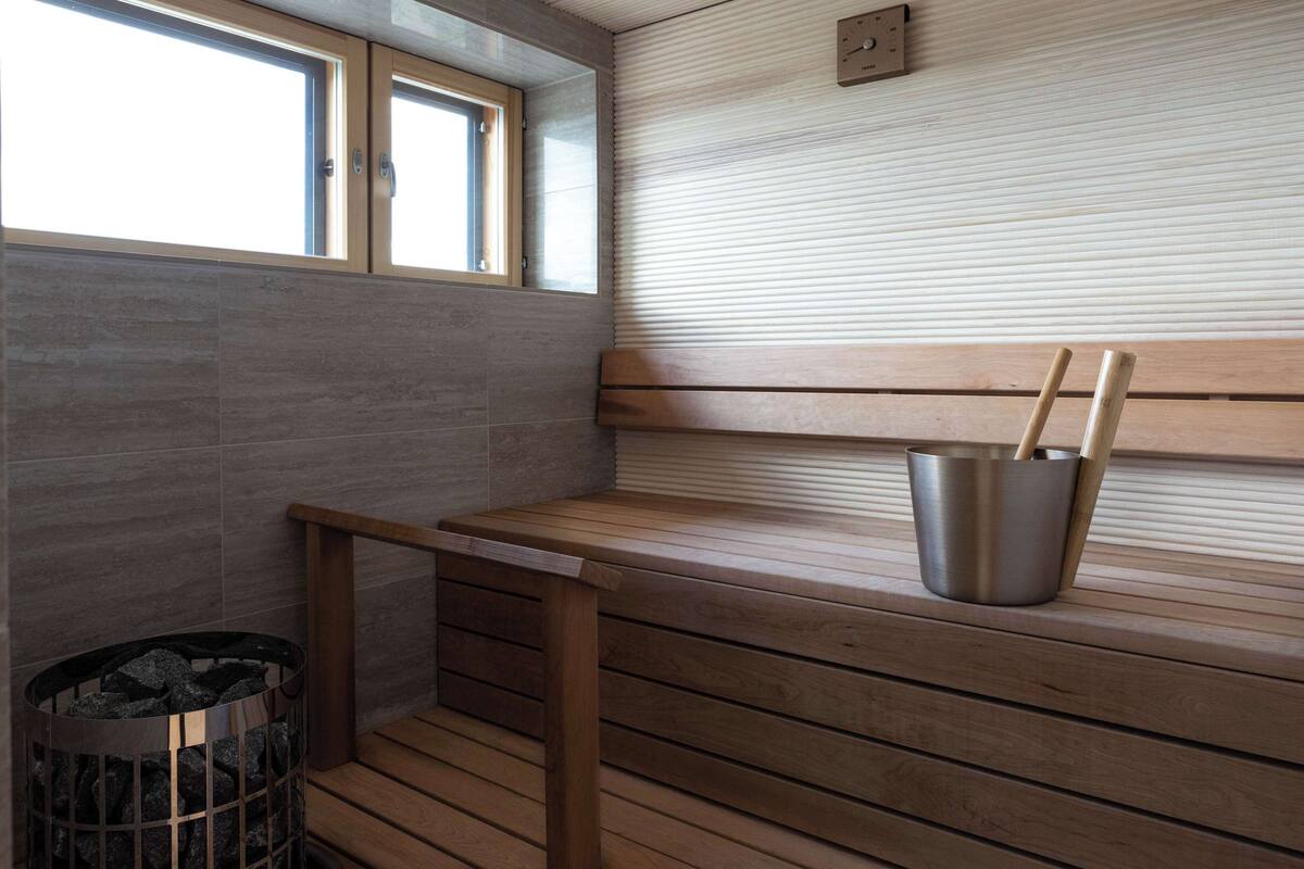 A sauna room with wooden benches, a metal bucket, and a trash bin.